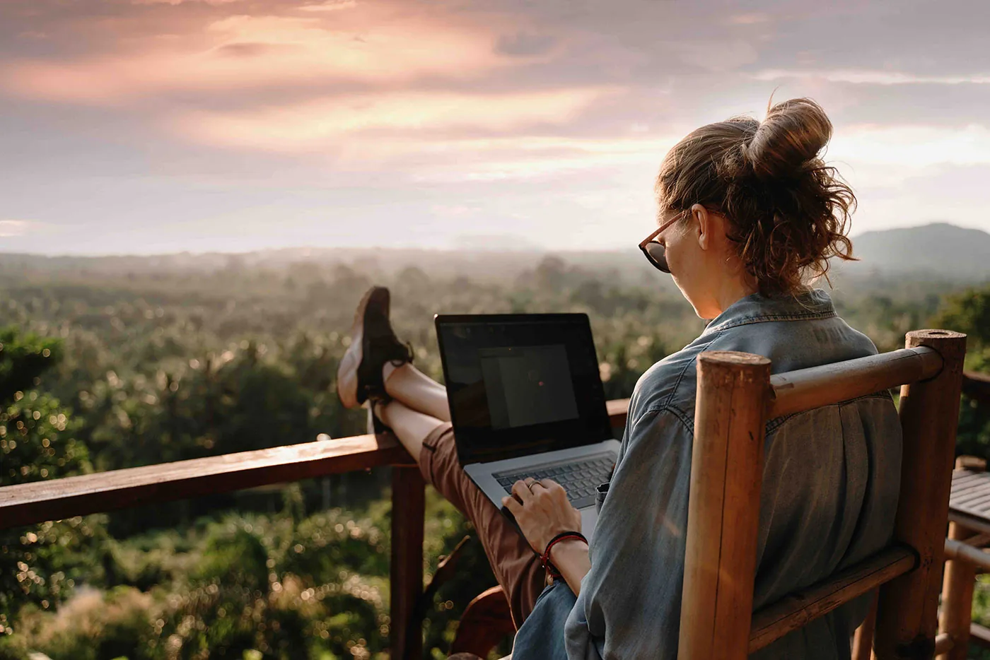 Investor reviewing a precious metals account on a laptop from a balcony overlooking hills at sunset