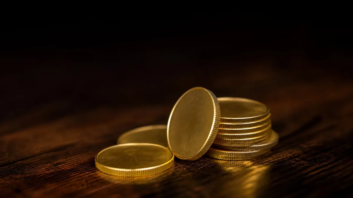 A small stack of gold coins on a dark wooden surface, lit from the side