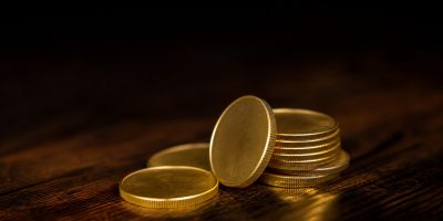 A small stack of gold coins on a dark wooden surface, lit from the side